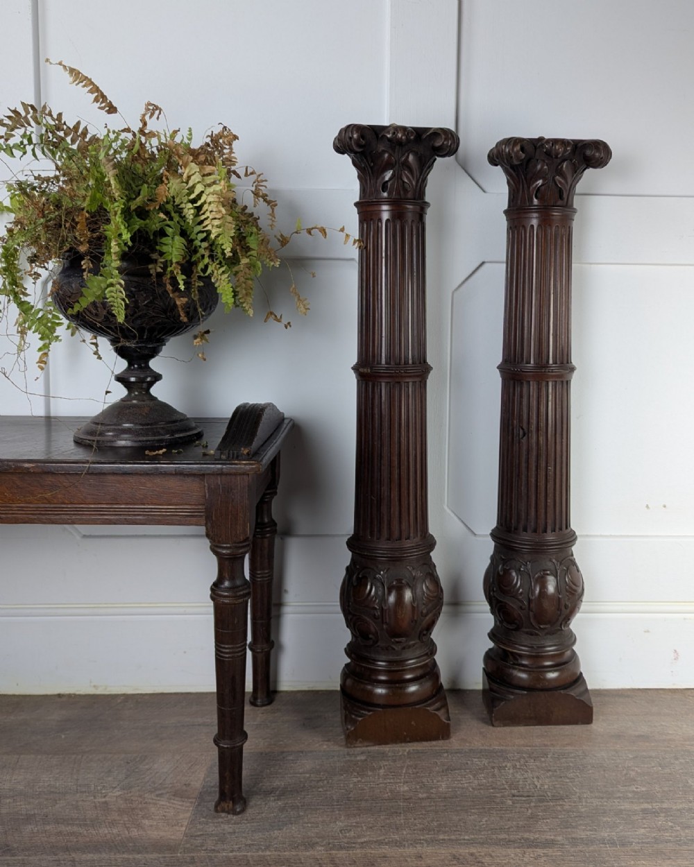 A pair of dark carved mahogany half columns featuring Corinthian capitals, reeded shafts, and carved bulbous bases.