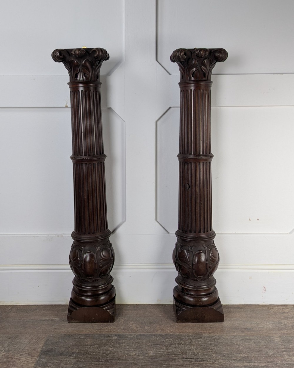 A pair of dark carved mahogany half columns featuring Corinthian capitals, reeded shafts, and carved bulbous bases. View X