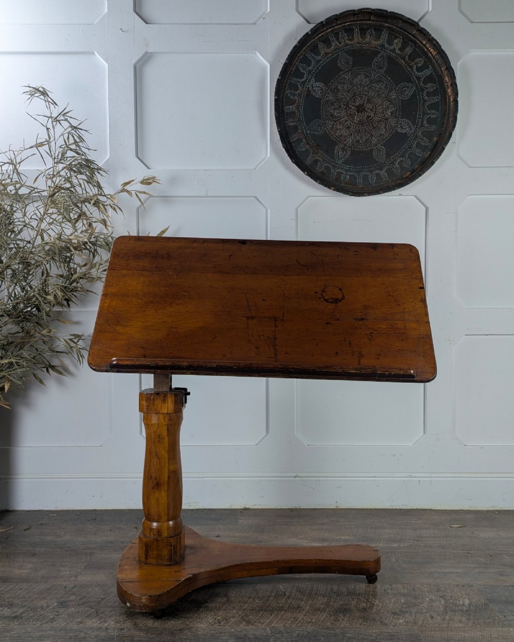 An early 20th-century pine reading table featuring an adjustable tilting top, a central turned support column, and a shaped base on small castors. View V