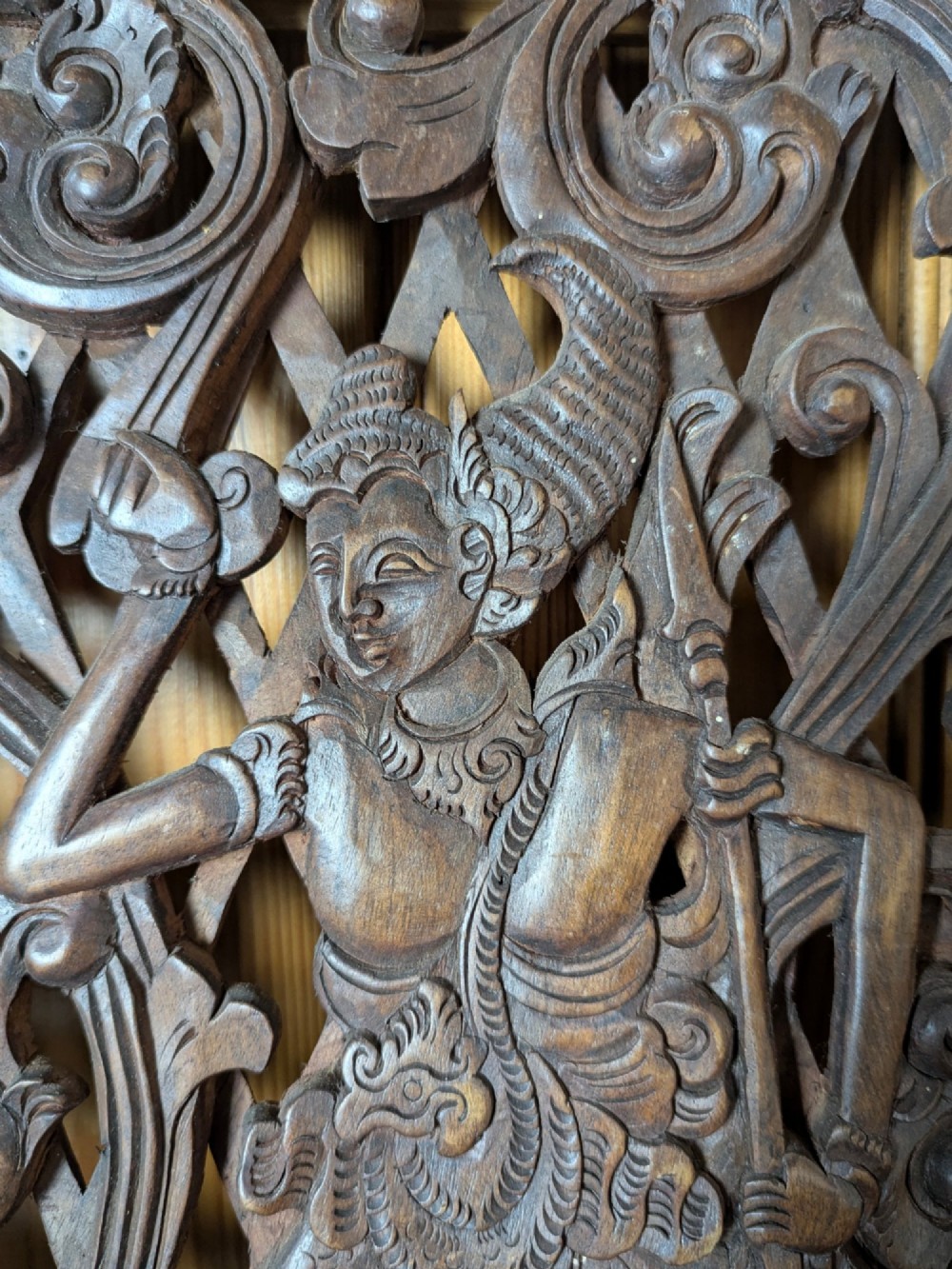 A rectangular dark teak wall panel hand-carved in high relief with an openwork Balinese mythological figure framed by intricate scrolling foliage. View III