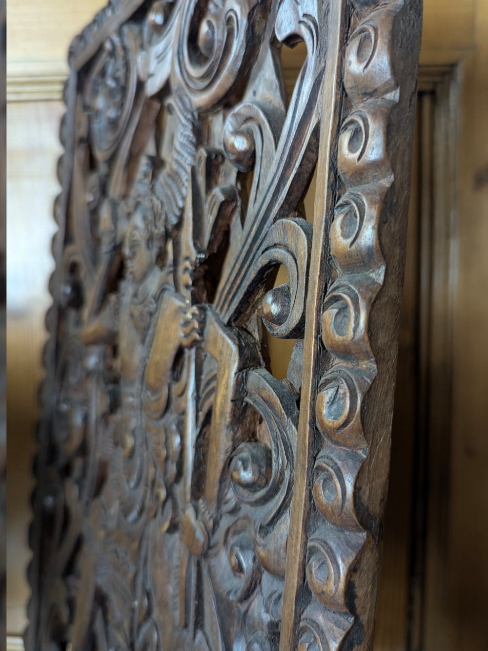 A rectangular dark teak wall panel hand-carved in high relief with an openwork Balinese mythological figure framed by intricate scrolling foliage. View VI