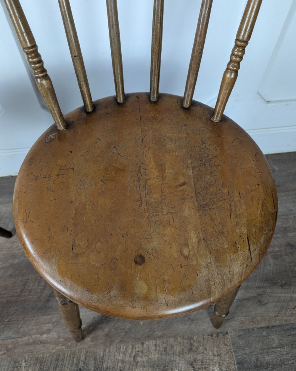 A pair of early twentieth-century wooden Dinco penny chairs featuring spindle backs, turned legs, curved stretchers, and shaped seats. View X