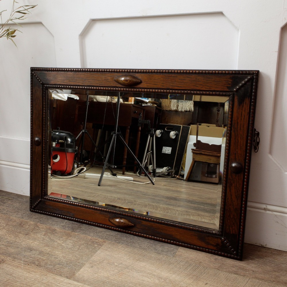 A rectangular dark oak wall mirror featuring a bevelled glass plate, beaded moulding around the frame, and applied wooden boss embellishments. View II