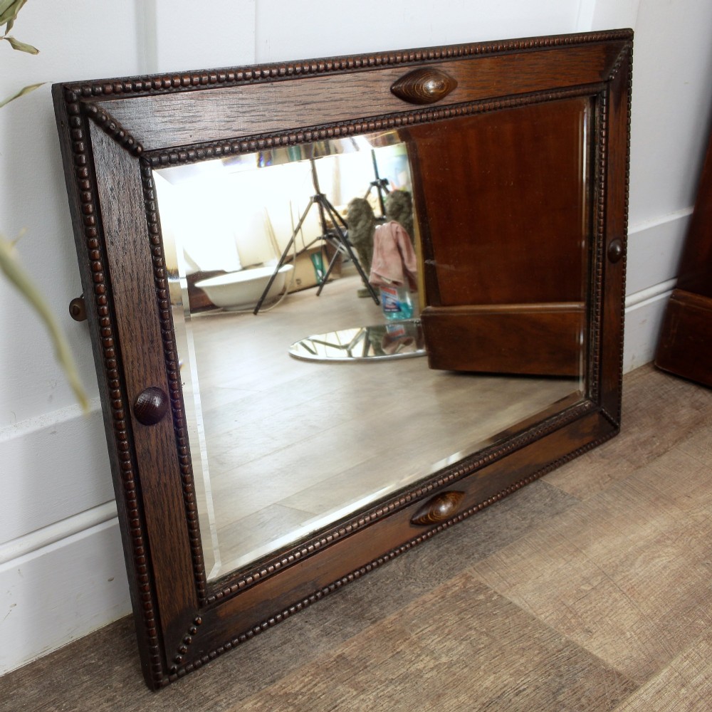 A rectangular dark oak wall mirror featuring a bevelled glass plate, beaded moulding around the frame, and applied wooden boss embellishments. View III