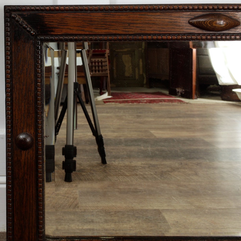 A rectangular dark oak wall mirror featuring a bevelled glass plate, beaded moulding around the frame, and applied wooden boss embellishments. View IV