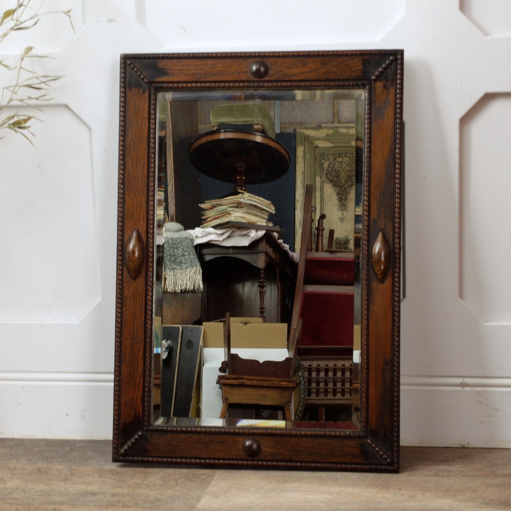 A rectangular dark oak wall mirror featuring a bevelled glass plate, beaded moulding around the frame, and applied wooden boss embellishments. View V