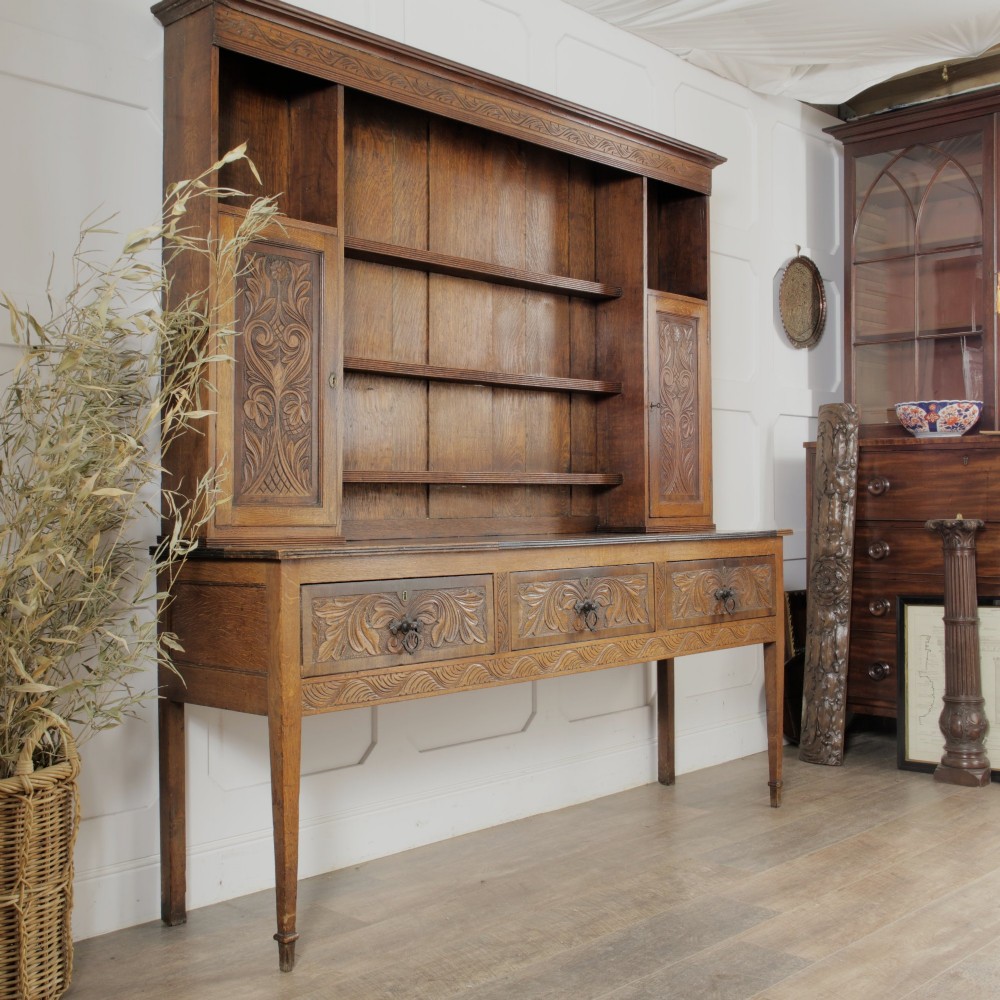 A mid-19th-century carved oak dresser featuring three relief-carved drawers, two side cupboards, tapered legs, and an upper display rack with open shelving. View II