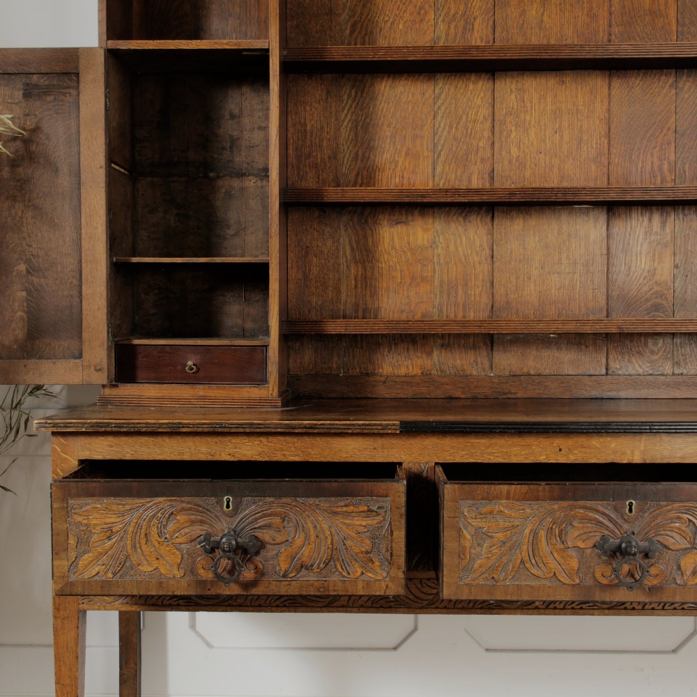 A mid-19th-century carved oak dresser featuring three relief-carved drawers, two side cupboards, tapered legs, and an upper display rack with open shelving. View V