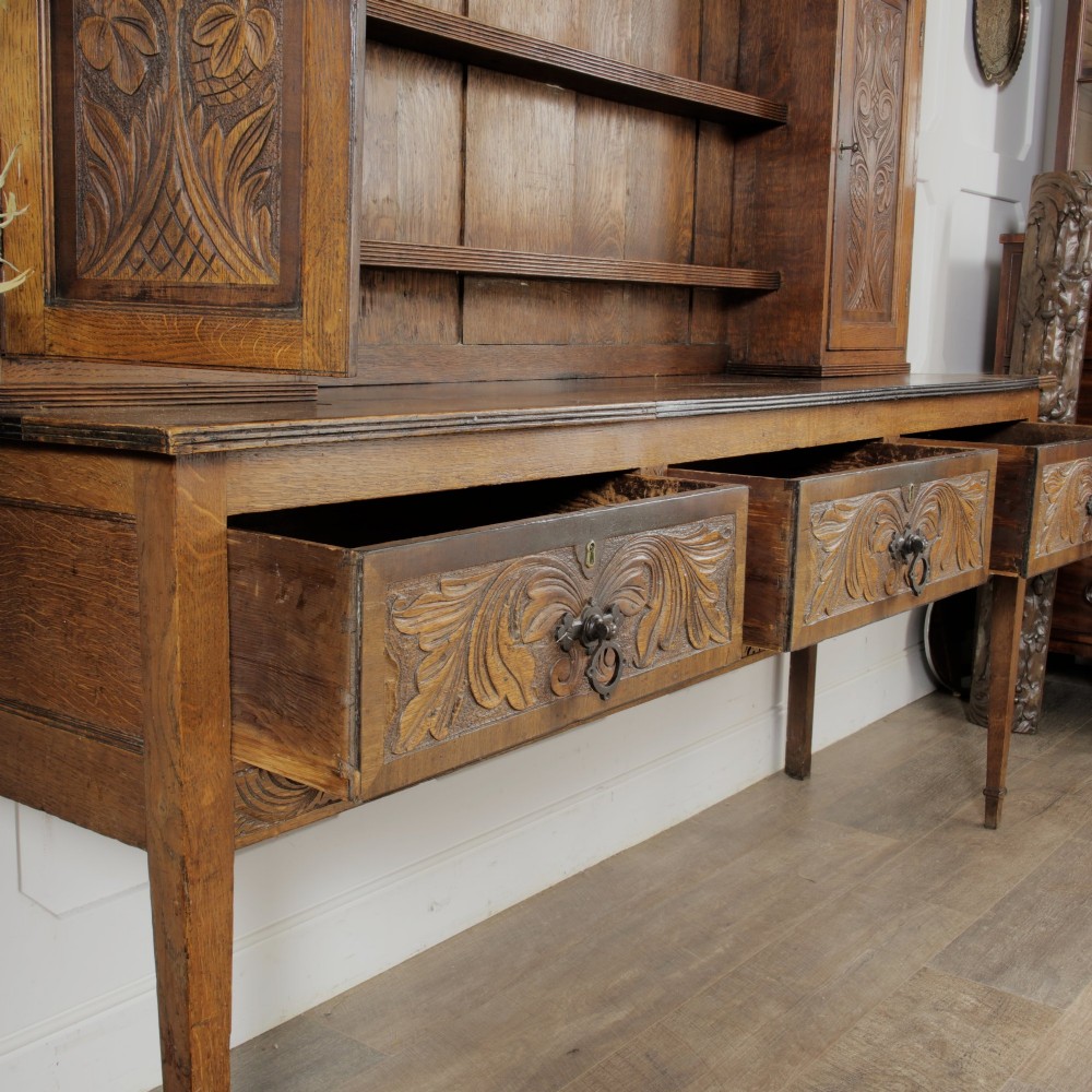 A mid-19th-century carved oak dresser featuring three relief-carved drawers, two side cupboards, tapered legs, and an upper display rack with open shelving. View VI