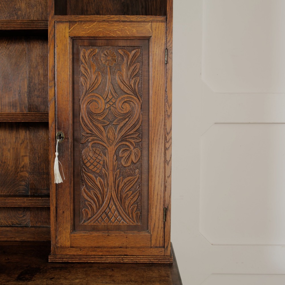 A mid-19th-century carved oak dresser featuring three relief-carved drawers, two side cupboards, tapered legs, and an upper display rack with open shelving. View VII