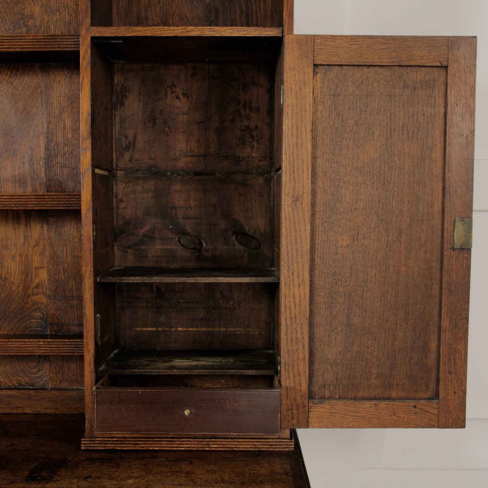 A mid-19th-century carved oak dresser featuring three relief-carved drawers, two side cupboards, tapered legs, and an upper display rack with open shelving. View VIII