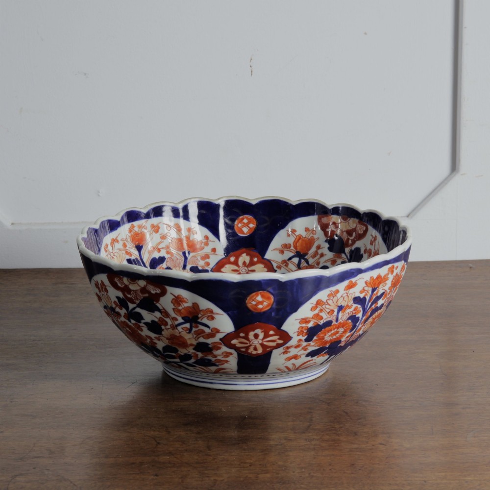 A round Japanese Imari porcelain bowl featuring scalloped edges and hand-painted floral motifs in cobalt blue, iron red, and white. View II