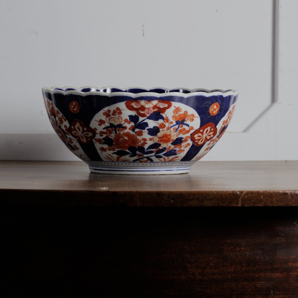 A round Japanese Imari porcelain bowl featuring scalloped edges and hand-painted floral motifs in cobalt blue, iron red, and white. View V