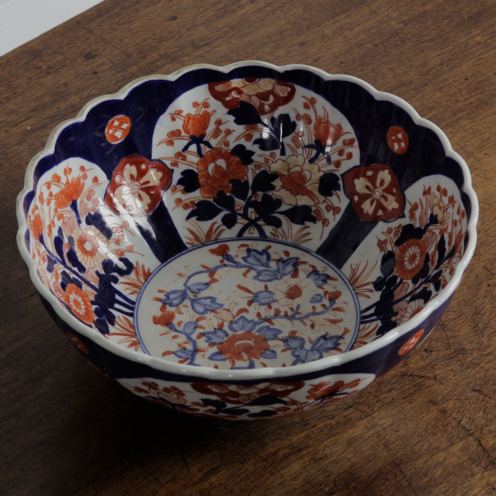 A round Japanese Imari porcelain bowl featuring scalloped edges and hand-painted floral motifs in cobalt blue, iron red, and white. View VI