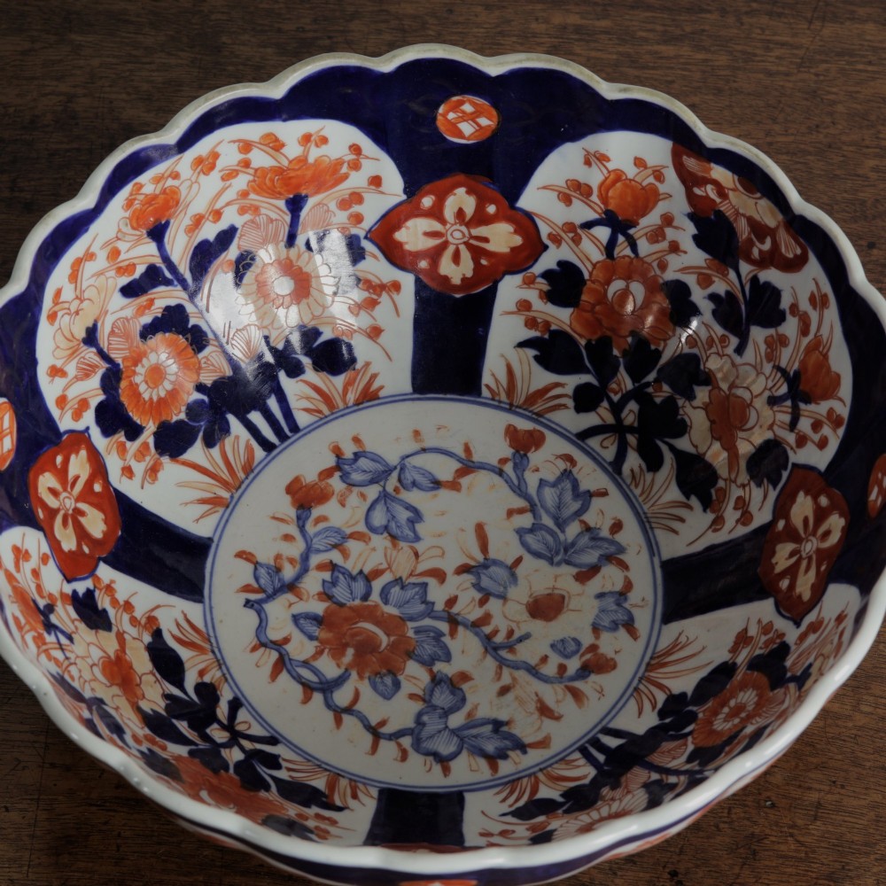 A round Japanese Imari porcelain bowl featuring scalloped edges and hand-painted floral motifs in cobalt blue, iron red, and white. View VII