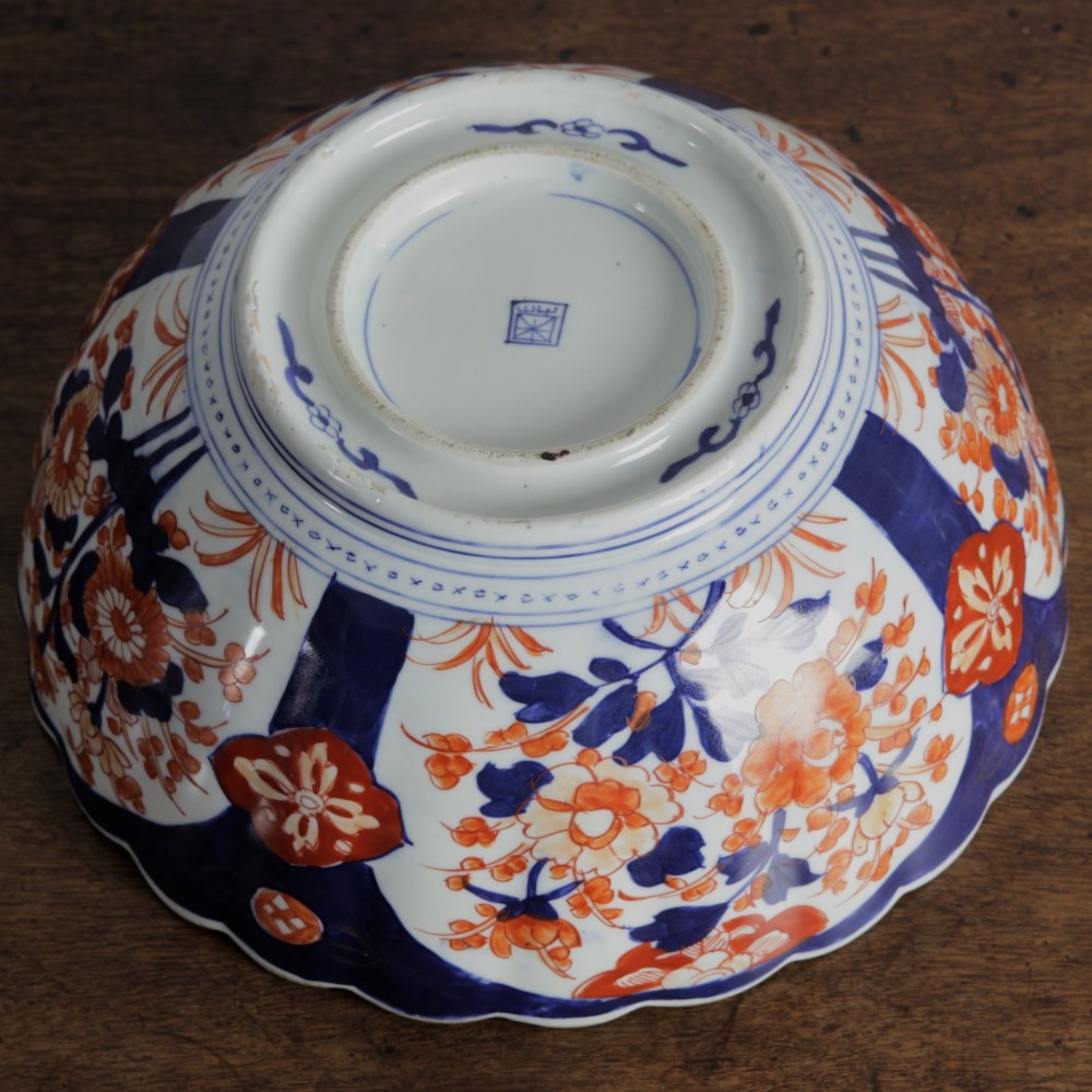 A round Japanese Imari porcelain bowl featuring scalloped edges and hand-painted floral motifs in cobalt blue, iron red, and white. View IX