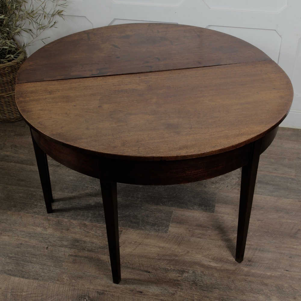 A pair of Georgian walnut demilune tables placed together to form a single round top with tapered legs.