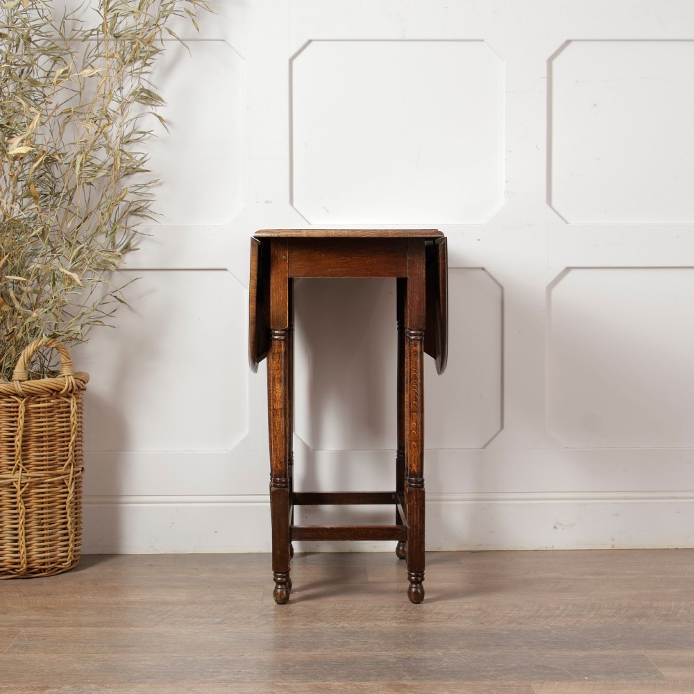 A small oak gateleg side table with turned legs, drop-down side flaps, and a warm brown wood finish. View X