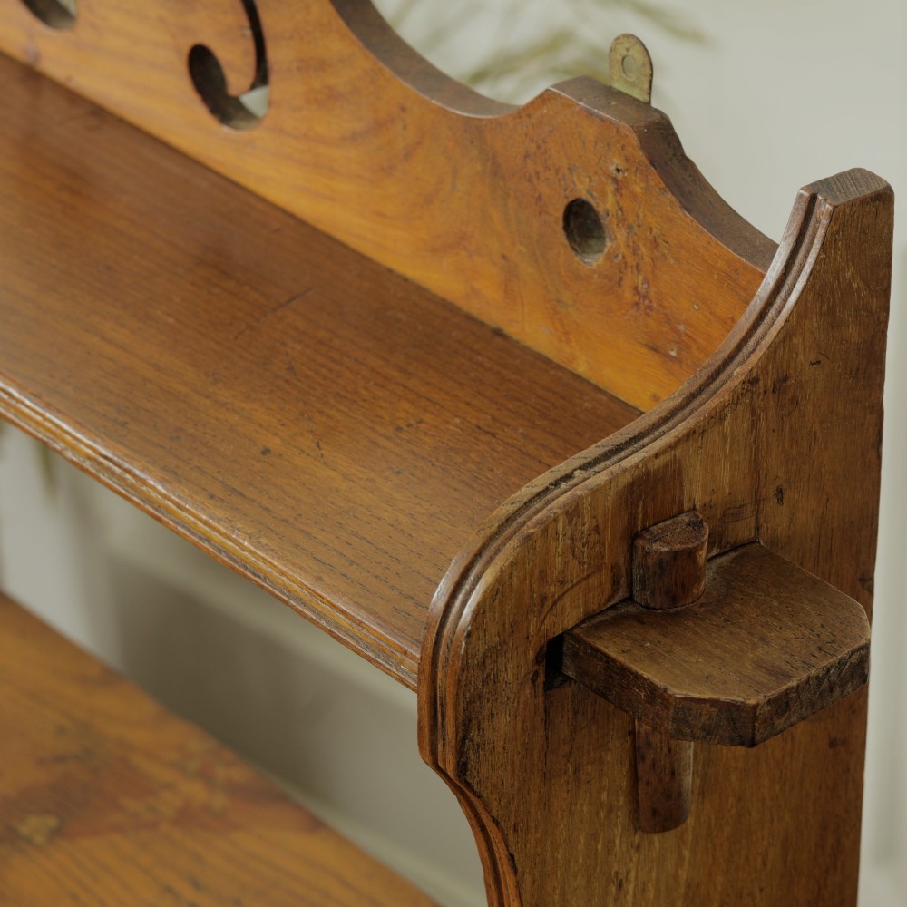 A three-tier warm brown wooden wall shelving unit featuring shaped side supports, wedged tenons, and a carved pierced cresting pediment. View VII