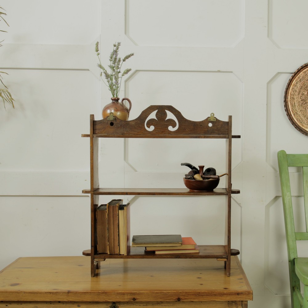 A three-tier warm brown wooden wall shelving unit featuring shaped side supports, wedged tenons, and a carved pierced cresting pediment. View VIII