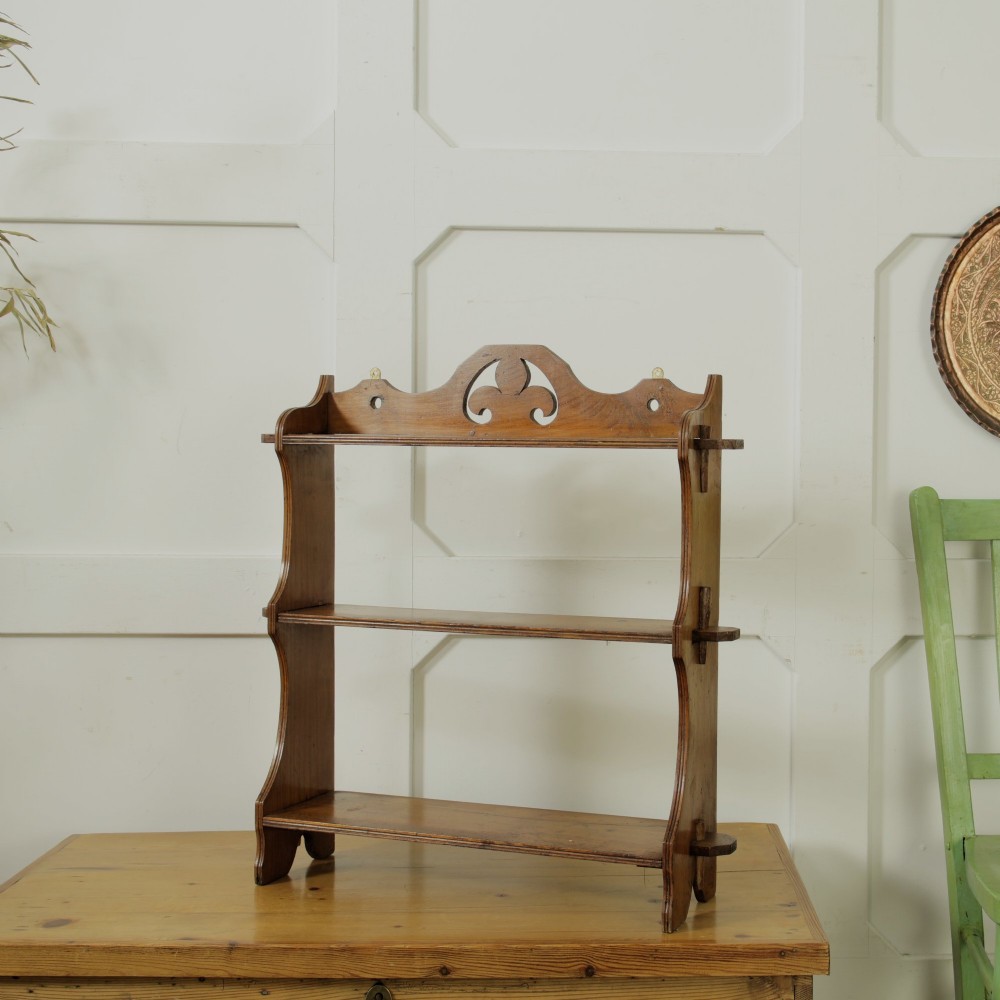 A three-tier warm brown wooden wall shelving unit featuring shaped side supports, wedged tenons, and a carved pierced cresting pediment. View IX
