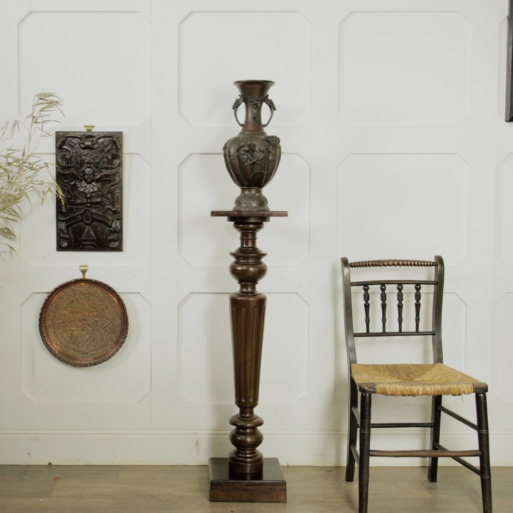 A dark turned mahogany plinth stand featuring a square top and base with a fluted central column. View II