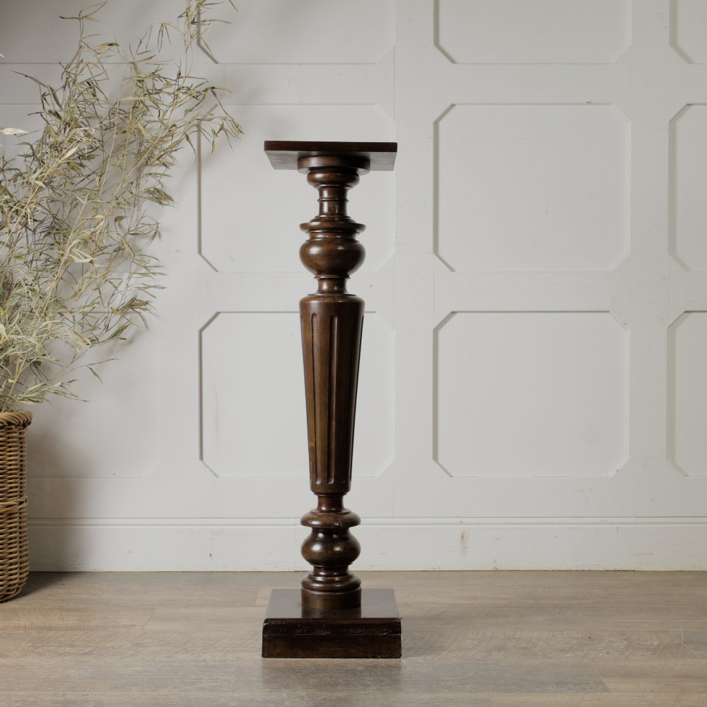 A dark turned mahogany plinth stand featuring a square top and base with a fluted central column.