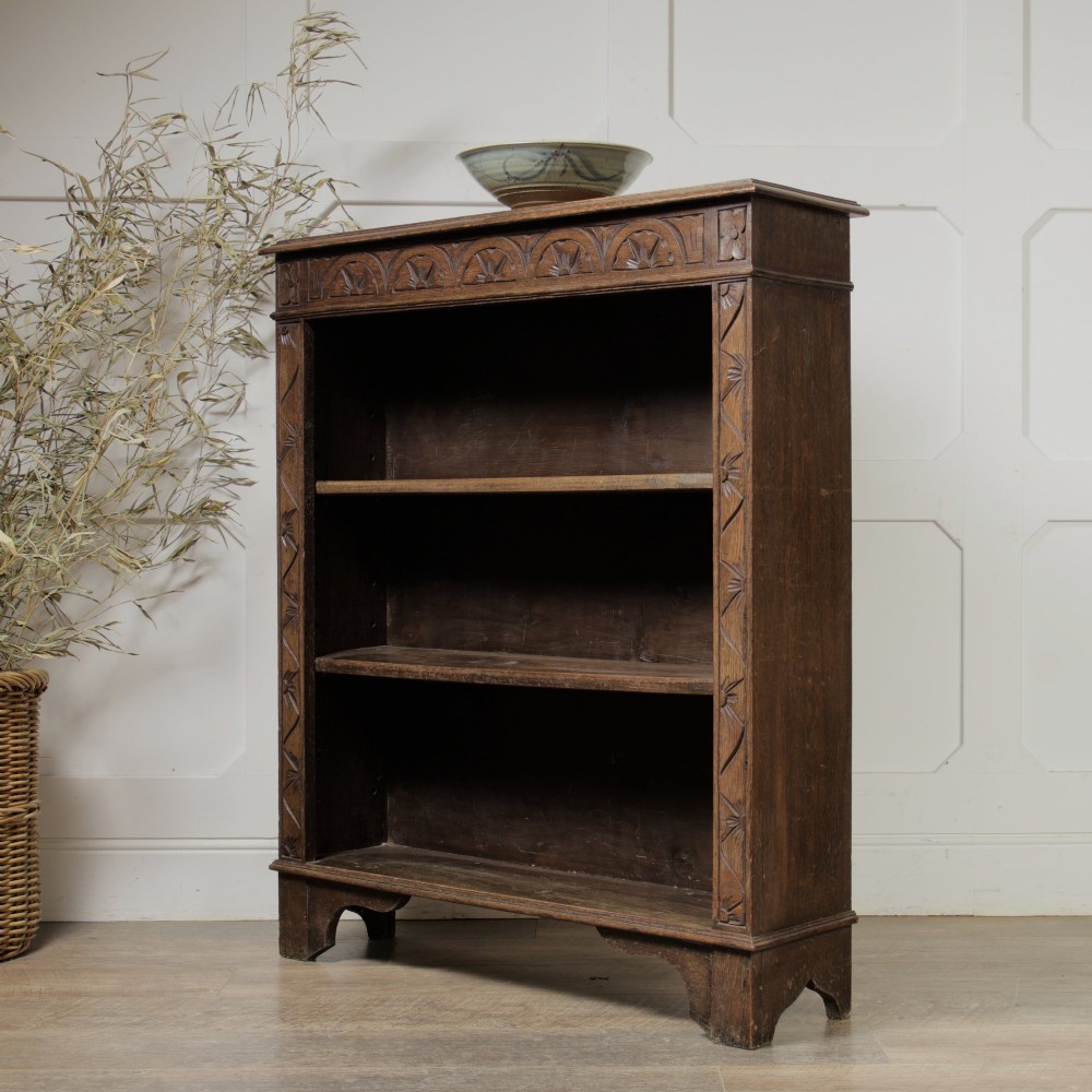 An early 20th-century dark oak open bookcase featuring a carved lunette frieze and three tiers of shelving. View II