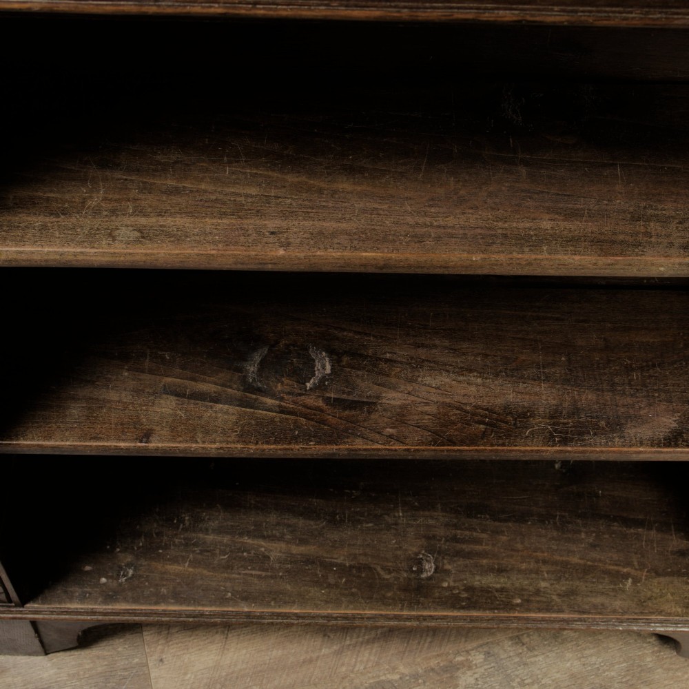 An early 20th-century dark oak open bookcase featuring a carved lunette frieze and three tiers of shelving. View IX