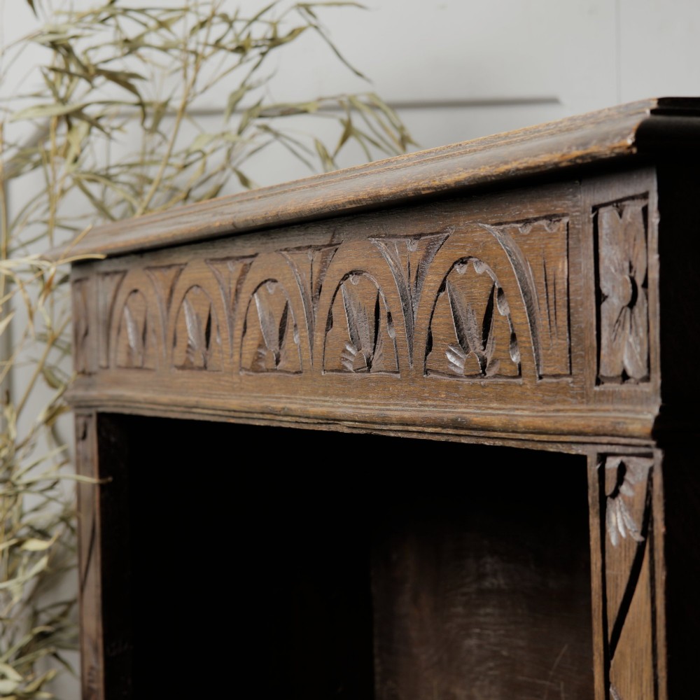 An early 20th-century dark oak open bookcase featuring a carved lunette frieze and three tiers of shelving. View X