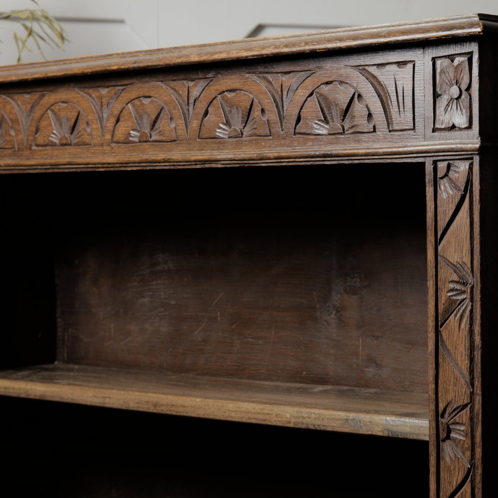 An early 20th-century dark oak open bookcase featuring a carved lunette frieze and three tiers of shelving. View XI