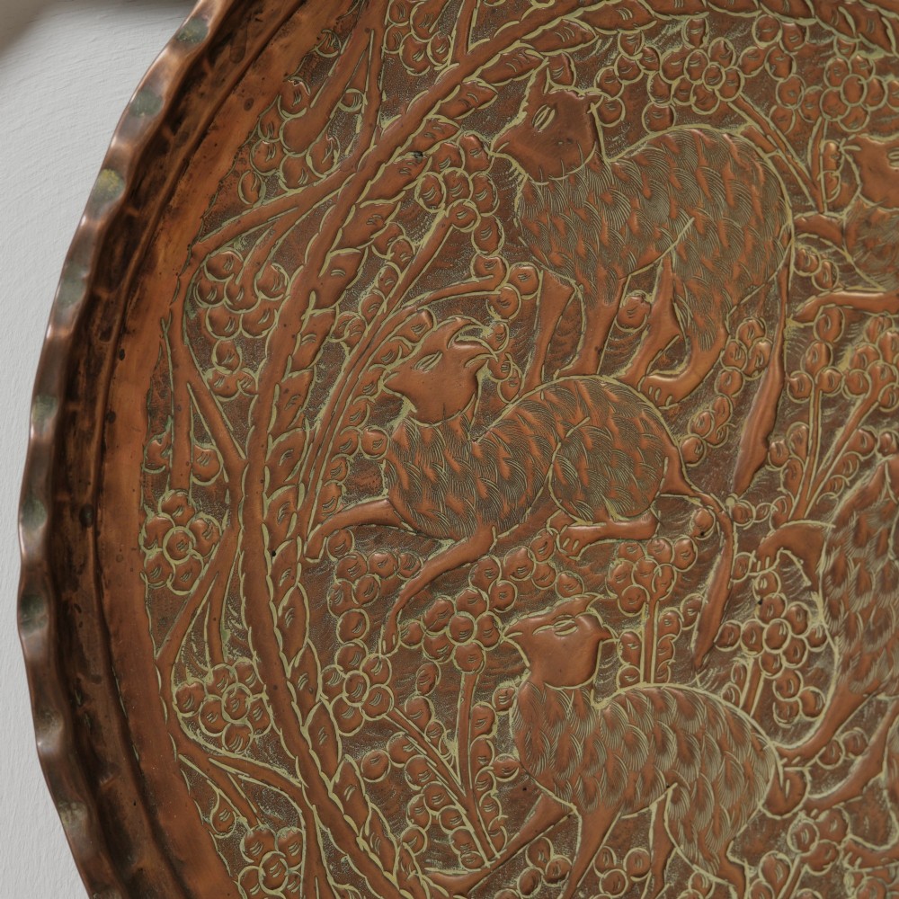 A circular hand-tooled copper charger tray featuring relief carvings of animals surrounded by foliage with a scalloped edge. View II