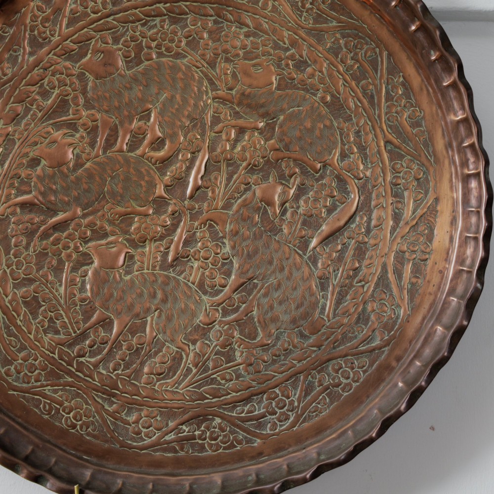 A circular hand-tooled copper charger tray featuring relief carvings of animals surrounded by foliage with a scalloped edge. View VII
