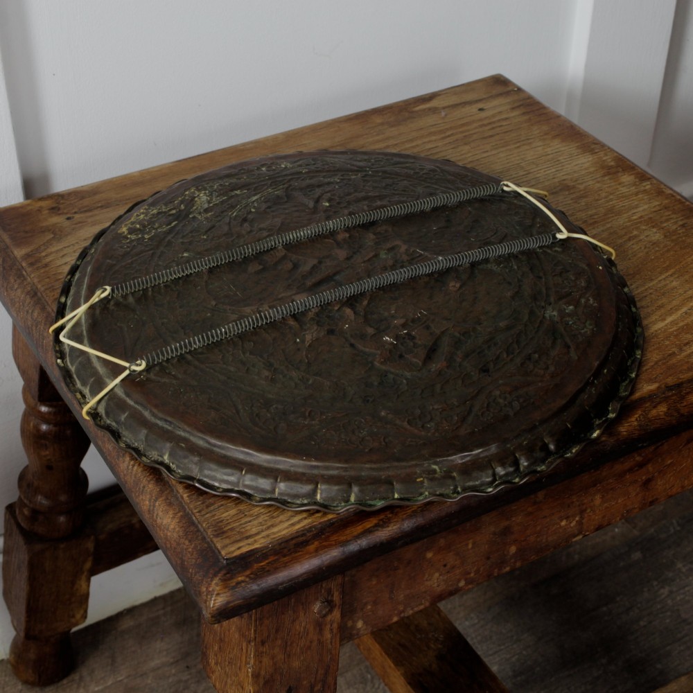 A circular hand-tooled copper charger tray featuring relief carvings of animals surrounded by foliage with a scalloped edge. View VIII