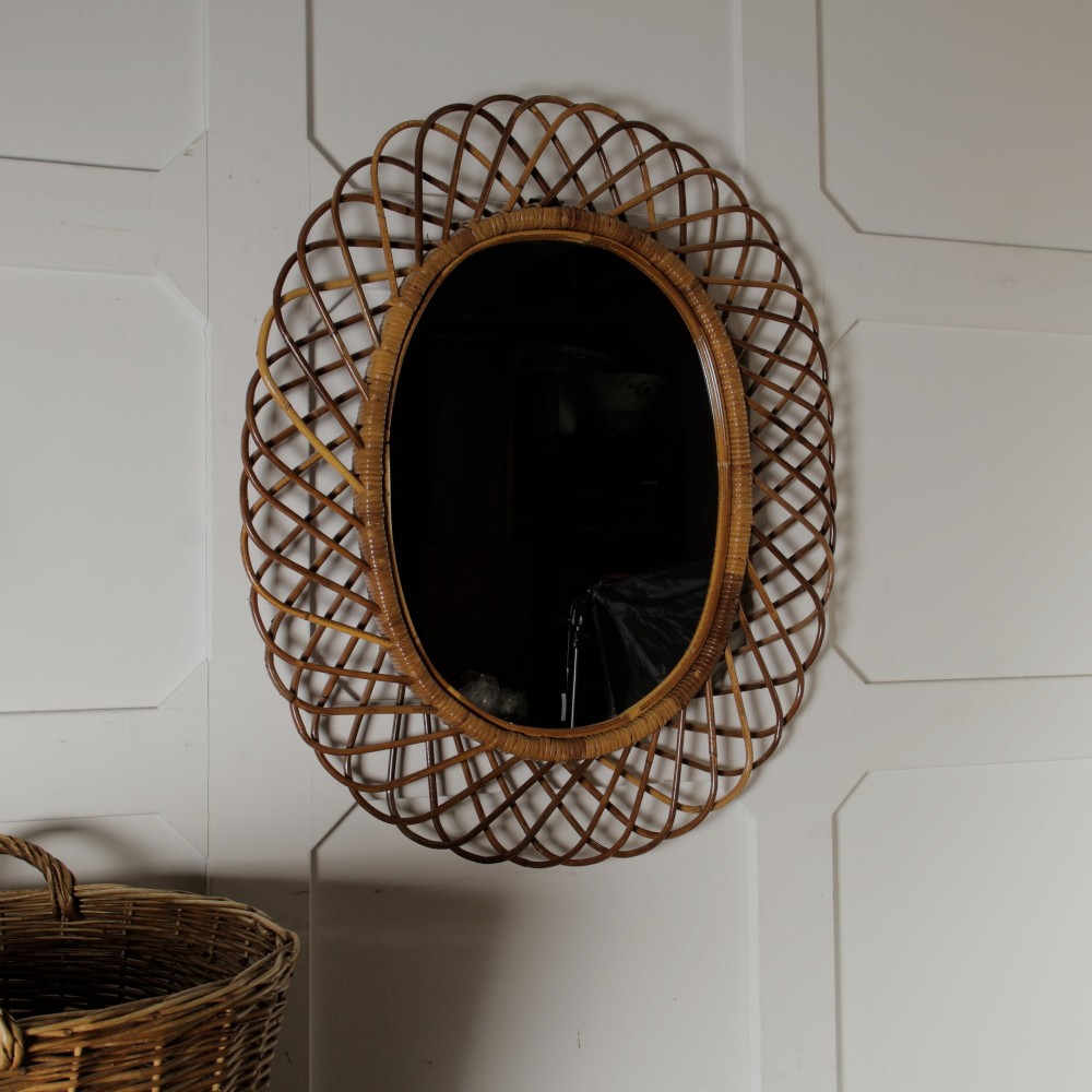 An oval mid-century wall mirror with an openwork outer frame crafted from woven, looped honey-toned rattan.