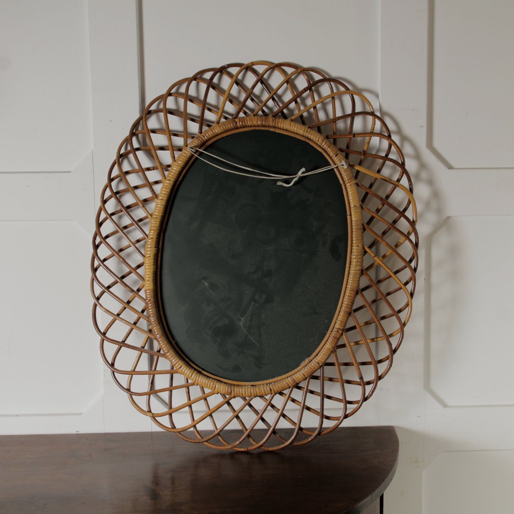 An oval mid-century wall mirror with an openwork outer frame crafted from woven, looped honey-toned rattan. View V