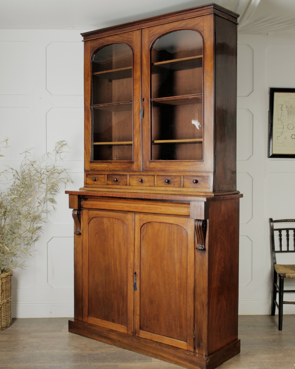 A two-tier Victorian mahogany chiffonier bookcase with arched glass double doors on the upper section and panelled cupboard doors on the lower base.