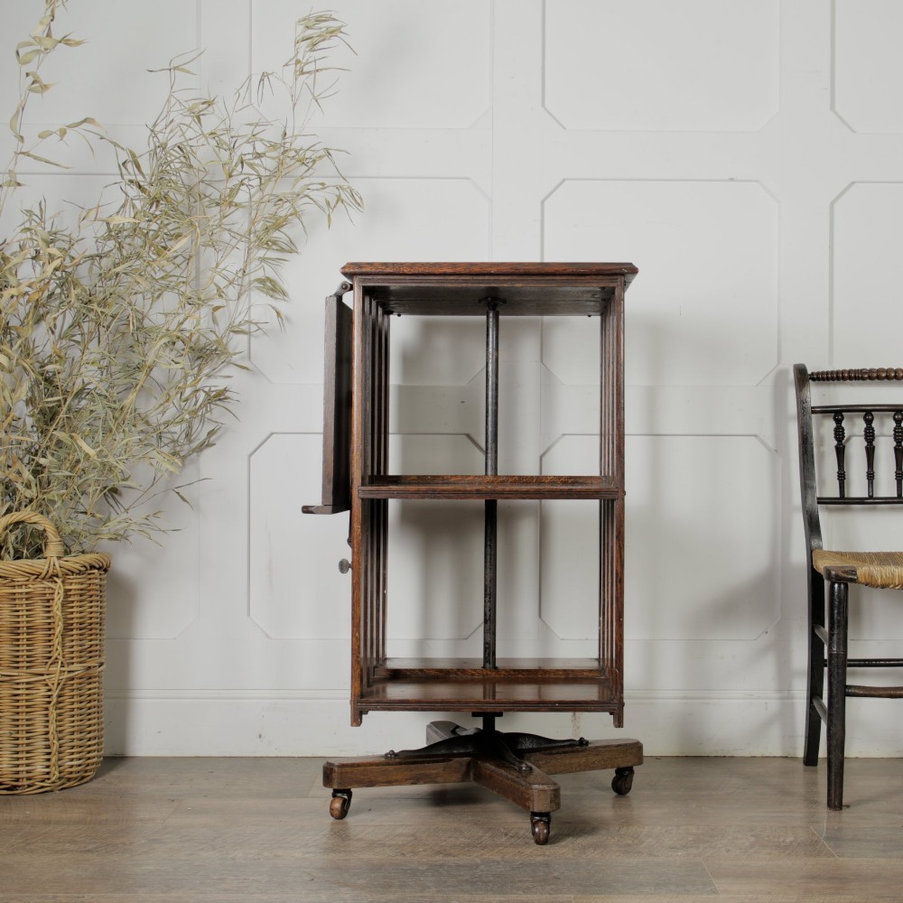 An Edwardian dark oak revolving bookcase featuring vertical slats, multiple shelf tiers, an adjustable folding reading rest, and a quadruped base on castors. View II