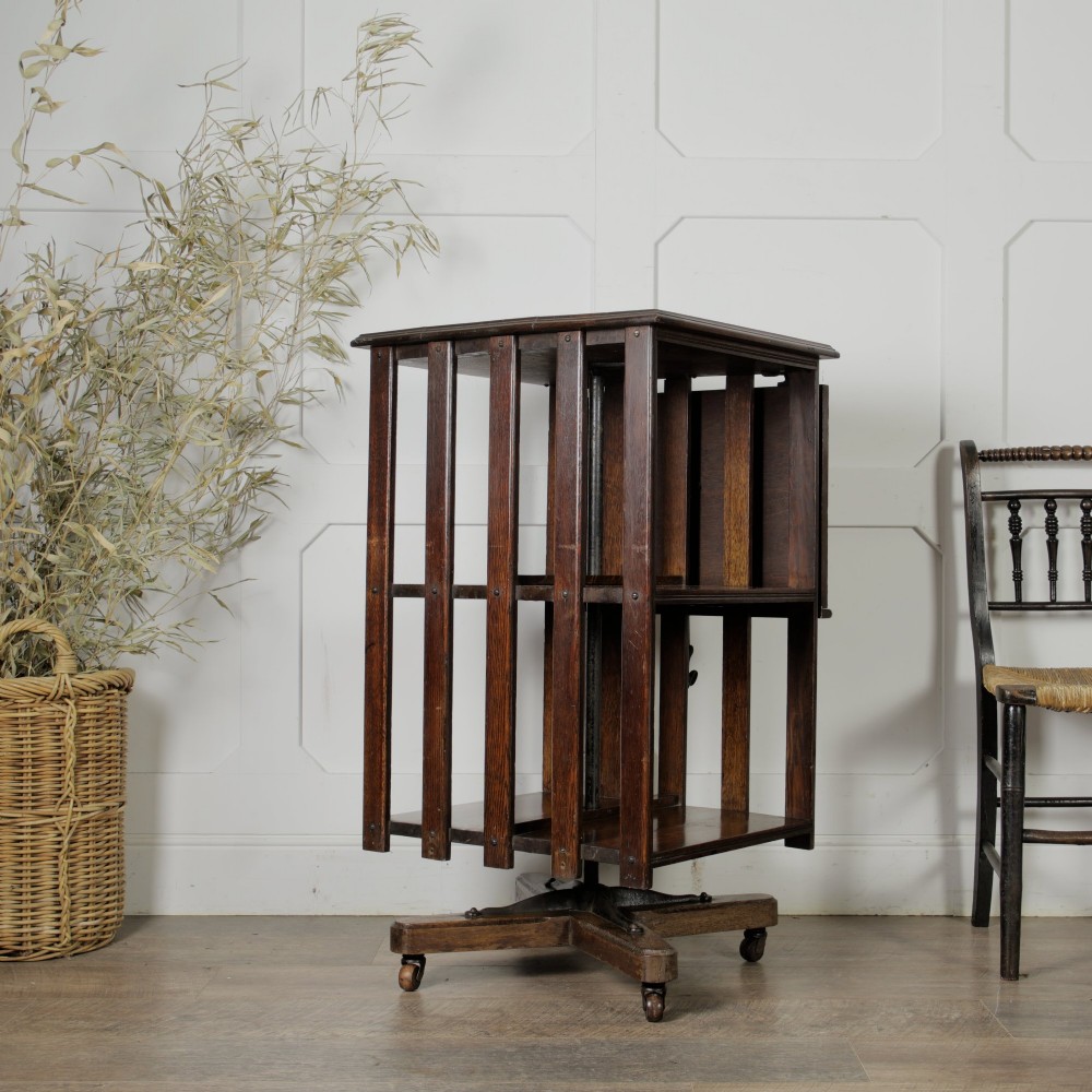 An Edwardian dark oak revolving bookcase featuring vertical slats, multiple shelf tiers, an adjustable folding reading rest, and a quadruped base on castors. View III