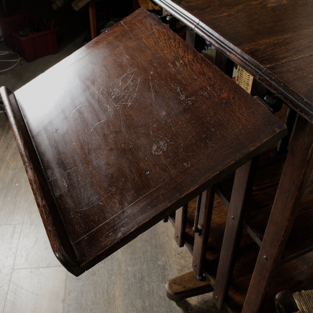 An Edwardian dark oak revolving bookcase featuring vertical slats, multiple shelf tiers, an adjustable folding reading rest, and a quadruped base on castors. View IV