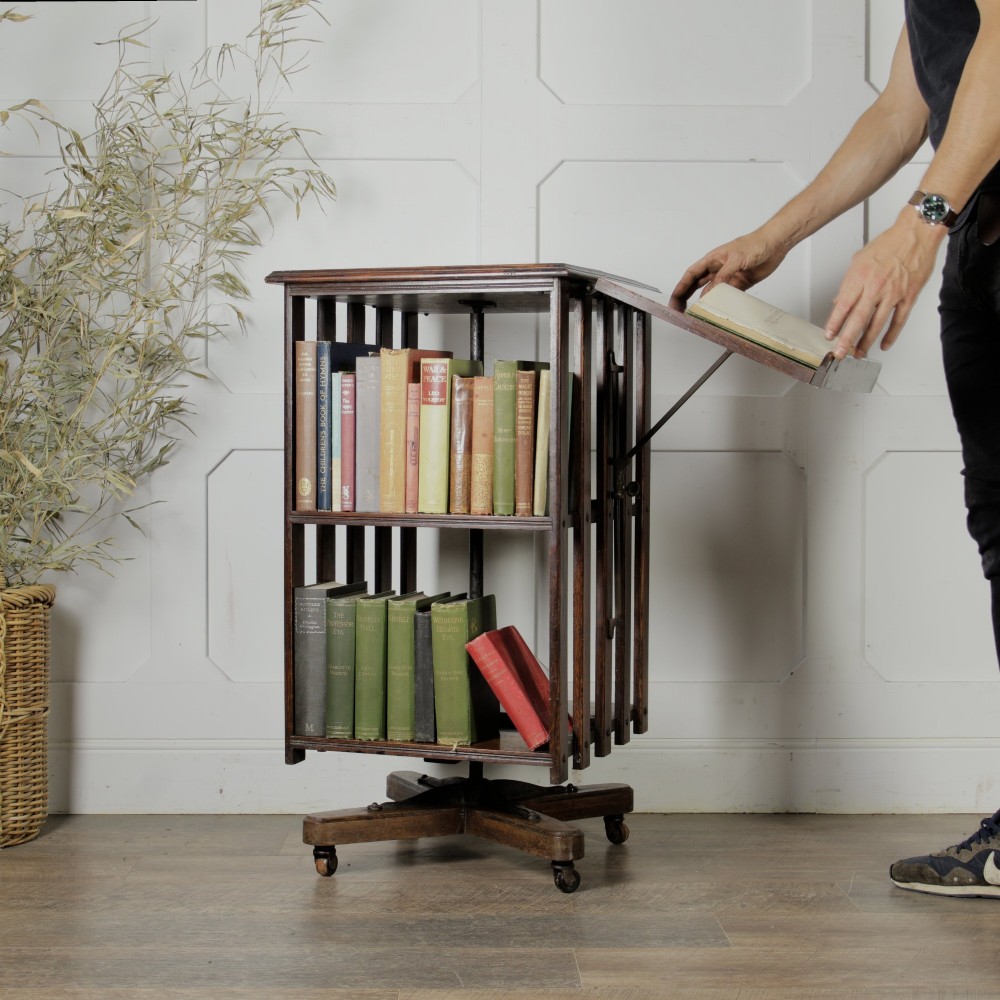 An Edwardian dark oak revolving bookcase featuring vertical slats, multiple shelf tiers, an adjustable folding reading rest, and a quadruped base on castors. View VII