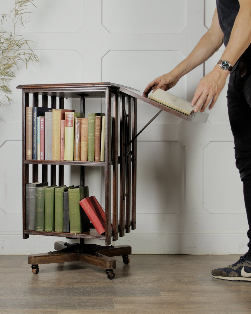 An Edwardian dark oak revolving bookcase featuring vertical slats, multiple shelf tiers, an adjustable folding reading rest, and a quadruped base on castors. View VIII