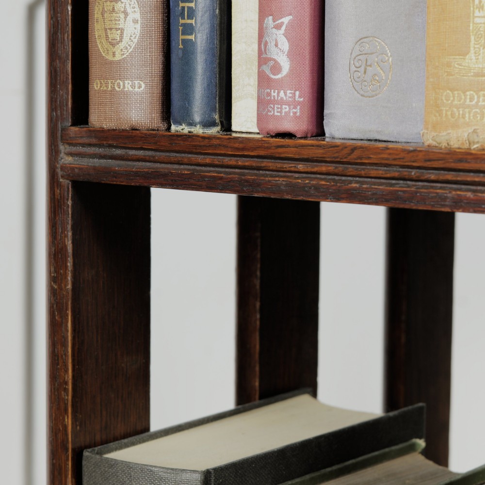 An Edwardian dark oak revolving bookcase featuring vertical slats, multiple shelf tiers, an adjustable folding reading rest, and a quadruped base on castors. View IX