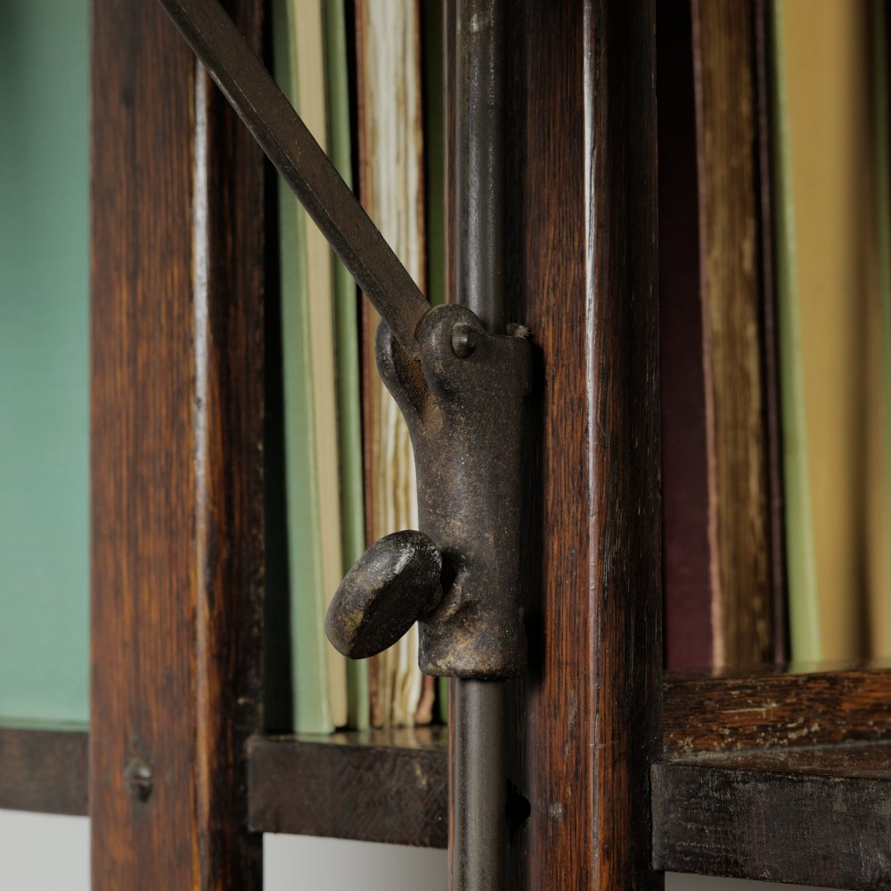 An Edwardian dark oak revolving bookcase featuring vertical slats, multiple shelf tiers, an adjustable folding reading rest, and a quadruped base on castors. View X
