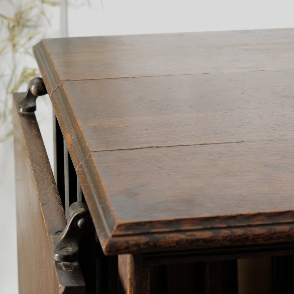 An Edwardian dark oak revolving bookcase featuring vertical slats, multiple shelf tiers, an adjustable folding reading rest, and a quadruped base on castors. View XII