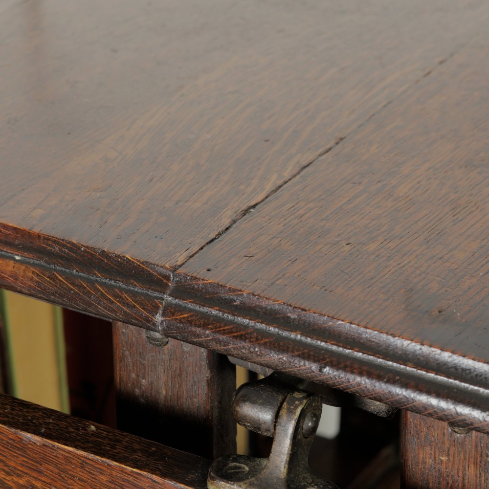 An Edwardian dark oak revolving bookcase featuring vertical slats, multiple shelf tiers, an adjustable folding reading rest, and a quadruped base on castors. View XIV