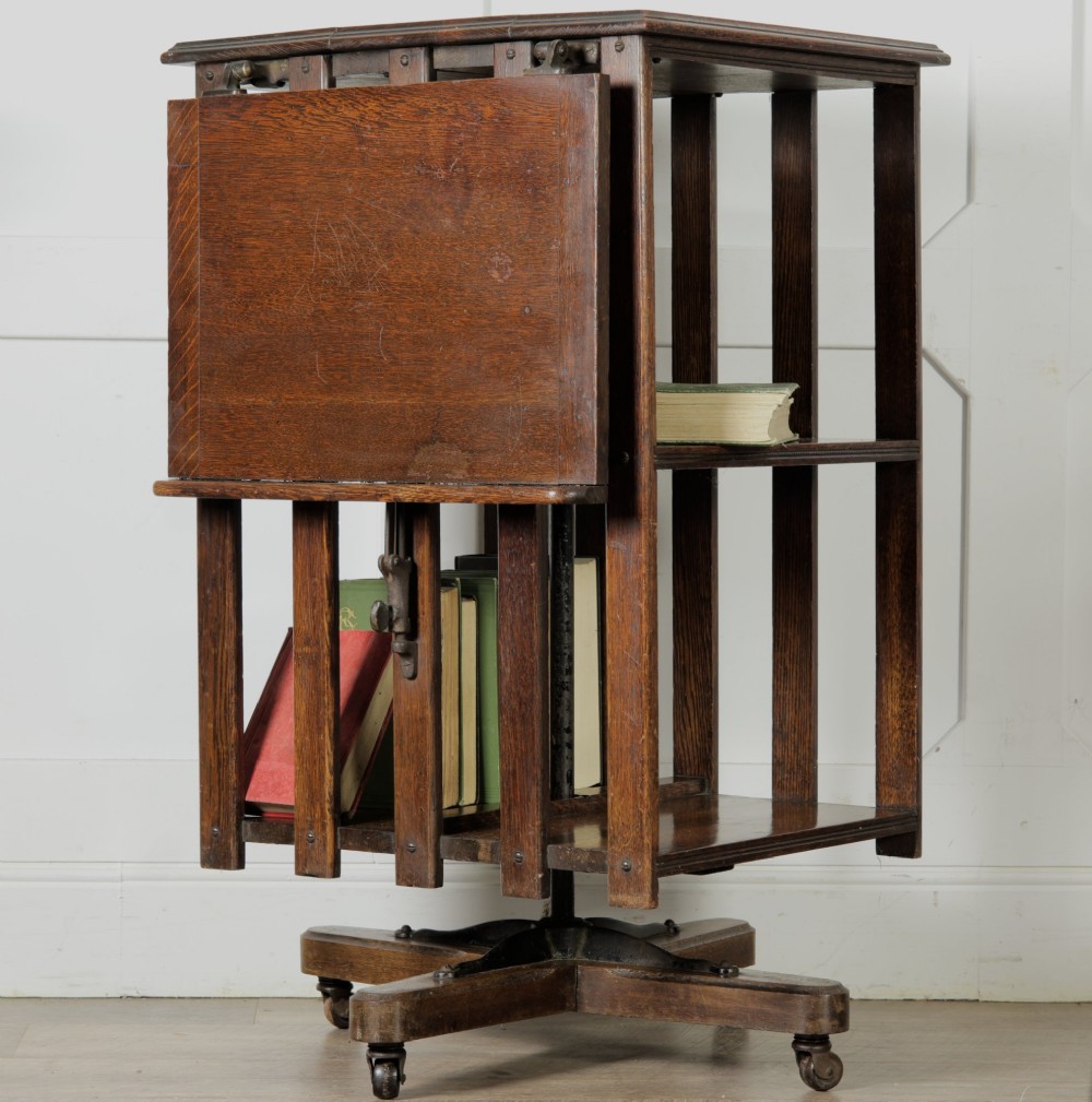 An Edwardian dark oak revolving bookcase featuring vertical slats, multiple shelf tiers, an adjustable folding reading rest, and a quadruped base on castors. View XV