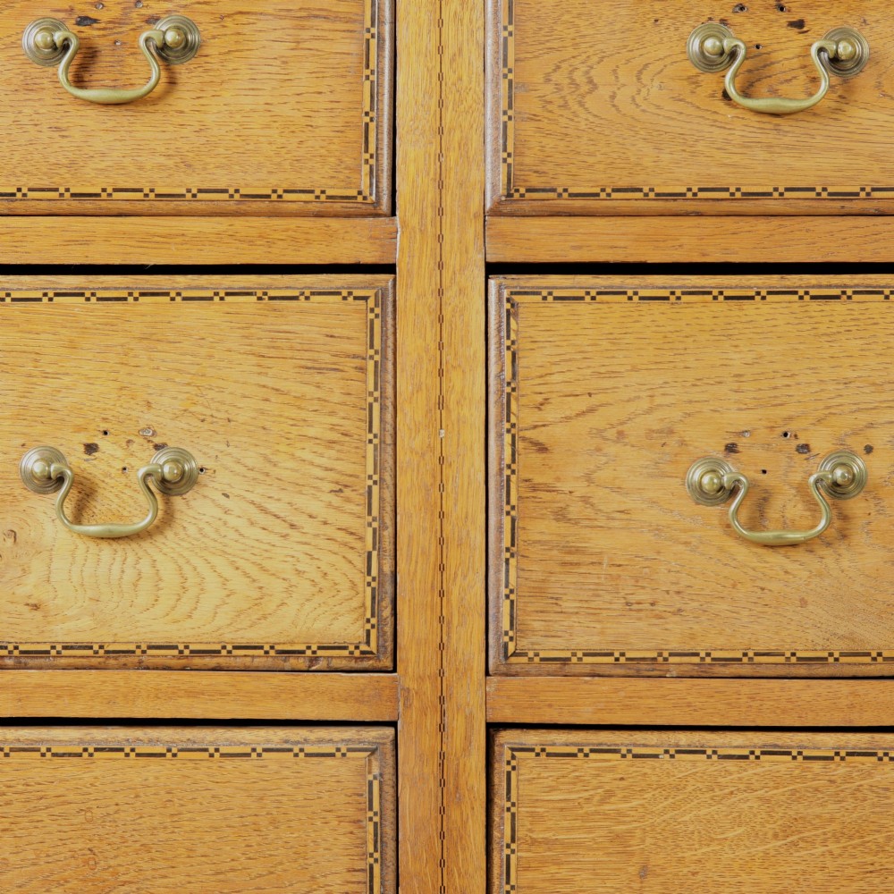 A solid honey-coloured oak dresser featuring a top section with open shelving and small side cupboards, set upon a base with six drawers and brass swan-neck handles. View II