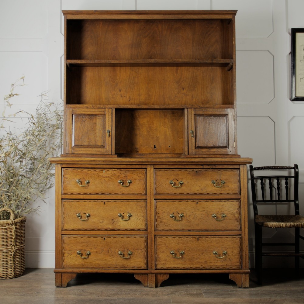 A solid honey-coloured oak dresser featuring a top section with open shelving and small side cupboards, set upon a base with six drawers and brass swan-neck handles. View VIII
