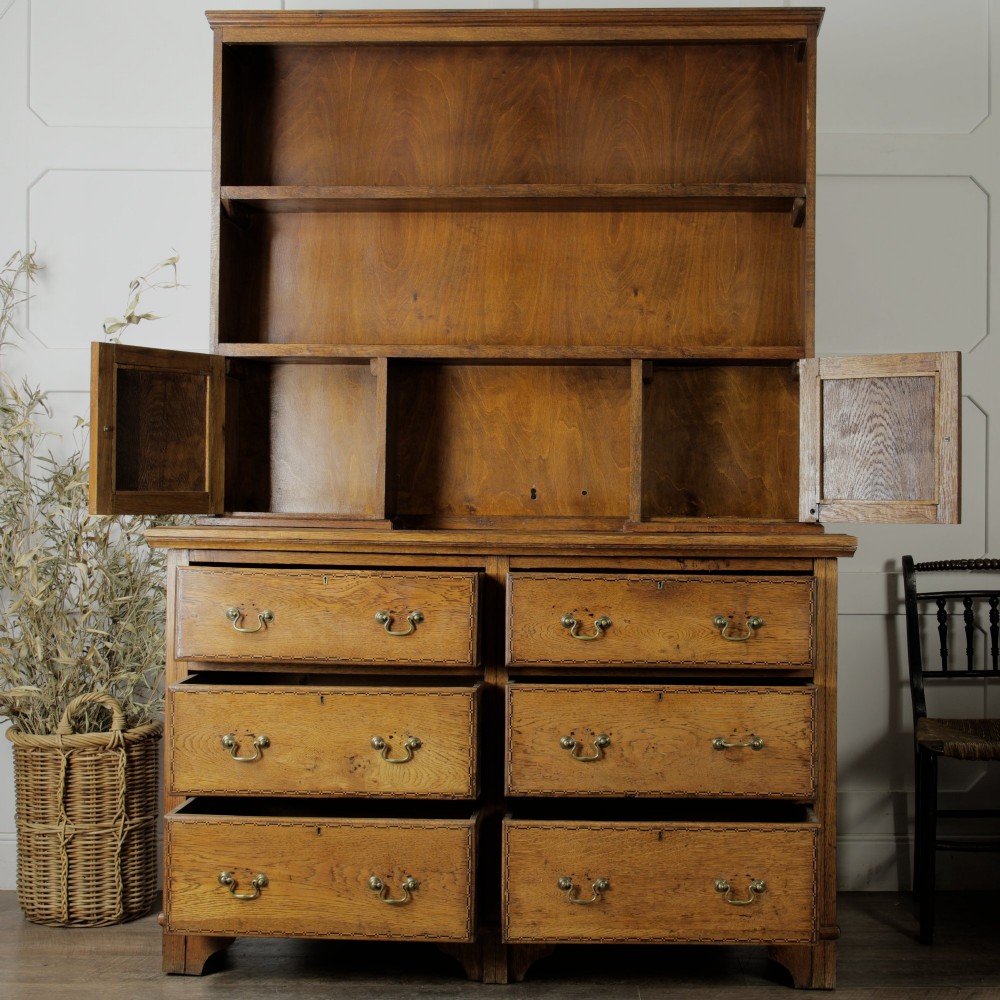 A solid honey-coloured oak dresser featuring a top section with open shelving and small side cupboards, set upon a base with six drawers and brass swan-neck handles. View X